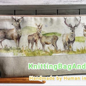 May include: A rectangular beige knitting bag with a watercolor print of deer in a grassy field. The bag has a zipper closure and a brown leather pull. The text "KnittingBagAndCase" is printed on the bag.