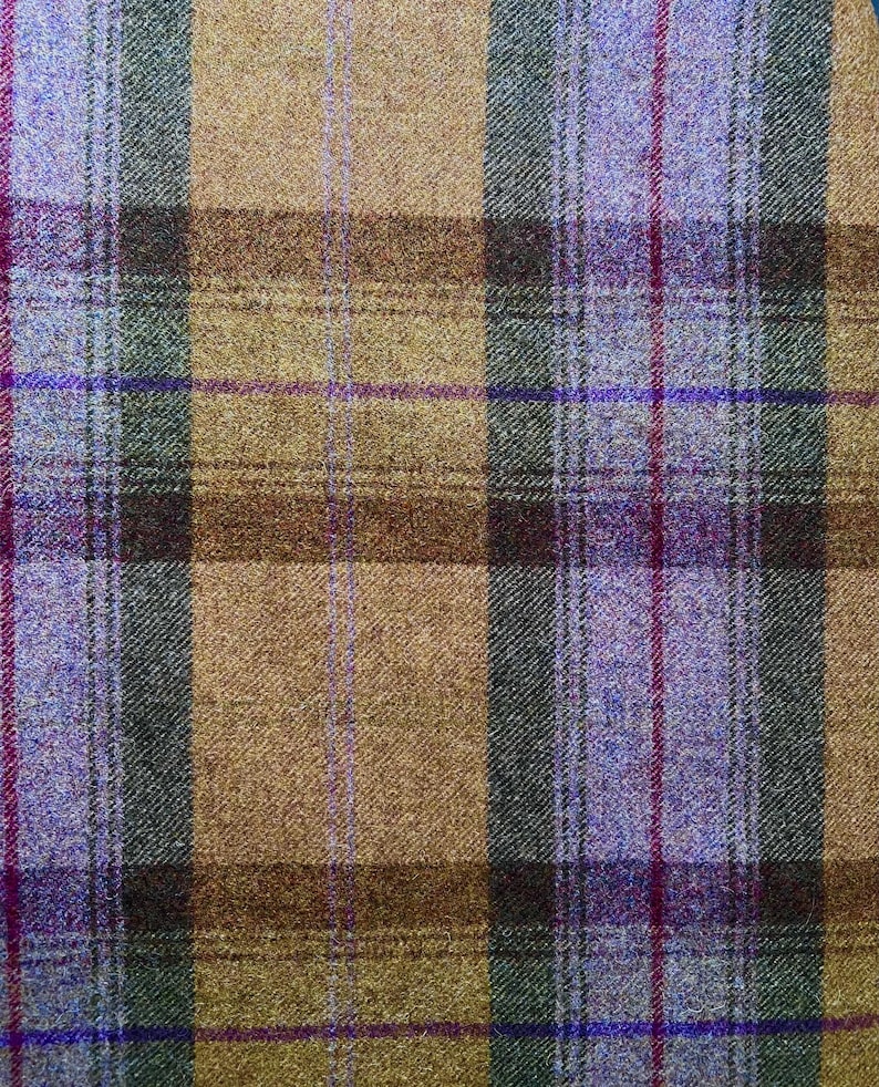 May include: A woven fabric featuring a plaid pattern with intersecting vertical and horizontal lines in shades of tan, dark brown, forest green, and bright purple, creating a textured surface with a visible cross-hatched weave structure.