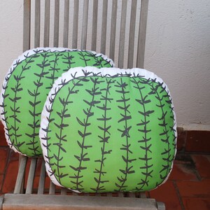 May include: Two green and white cactus-shaped throw pillows with black stitching on a wooden chair.