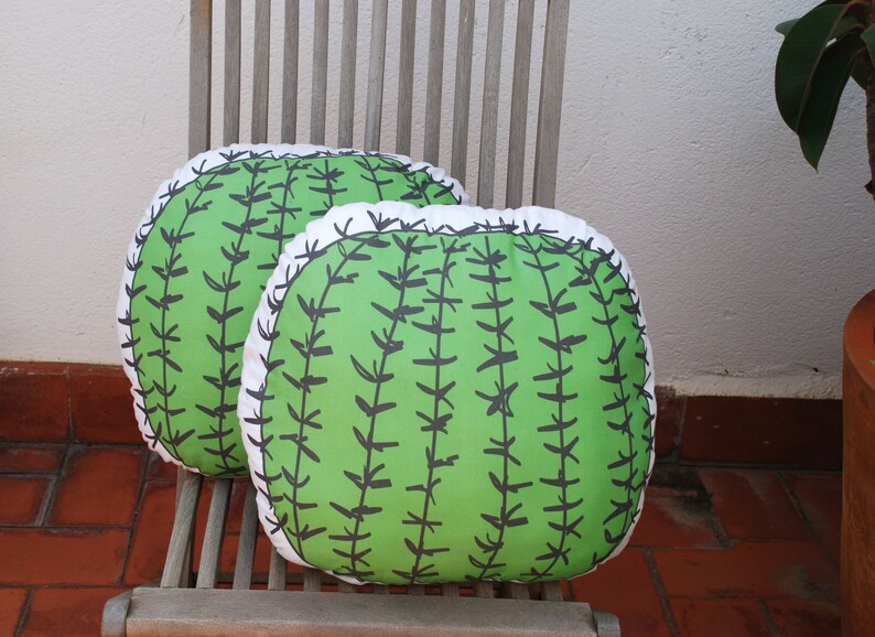 May include: Two green and white cactus-shaped throw pillows with black stitching on a wooden chair.
