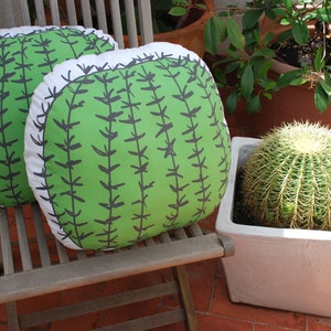 May include: Two green and white cactus-patterned throw pillows on a wooden chair. The pillows are sitting on a wooden chair with a white cushion.