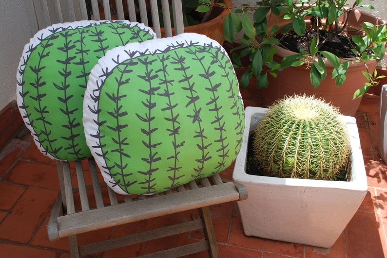 May include: Two green and white cactus-patterned throw pillows on a wooden chair. The pillows are sitting on a wooden chair with a white cushion.