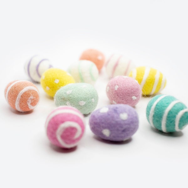 Peut inclure: Une collection d'œufs de Pâques en feutre colorés avec des pois blancs et des rayures. Les œufs sont disposés sur une surface blanche.