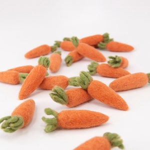 May include: A collection of felt carrots in various sizes, with green tops, arranged on a white surface. The carrots are a light orange color and have a soft, fuzzy texture.