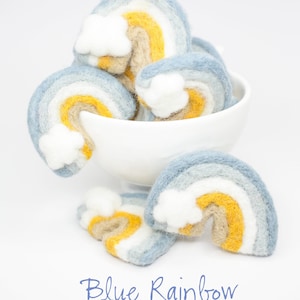 May include: A bowl filled with felt rainbow ornaments. The rainbows are blue, white, yellow, and brown. The ornaments have a cloud shape on the top.