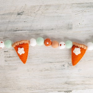 May include: A felt garland with orange and brown pie slices, white and green felt balls, and brown felt balls with white polka dots.