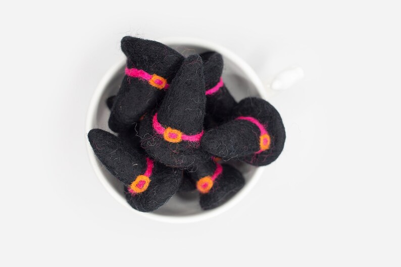 May include: A bowl filled with felt witch hats. The hats are black with pink and orange trim.
