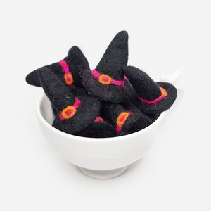 May include: A white ceramic bowl filled with black felt witch hats with pink and orange trim.
