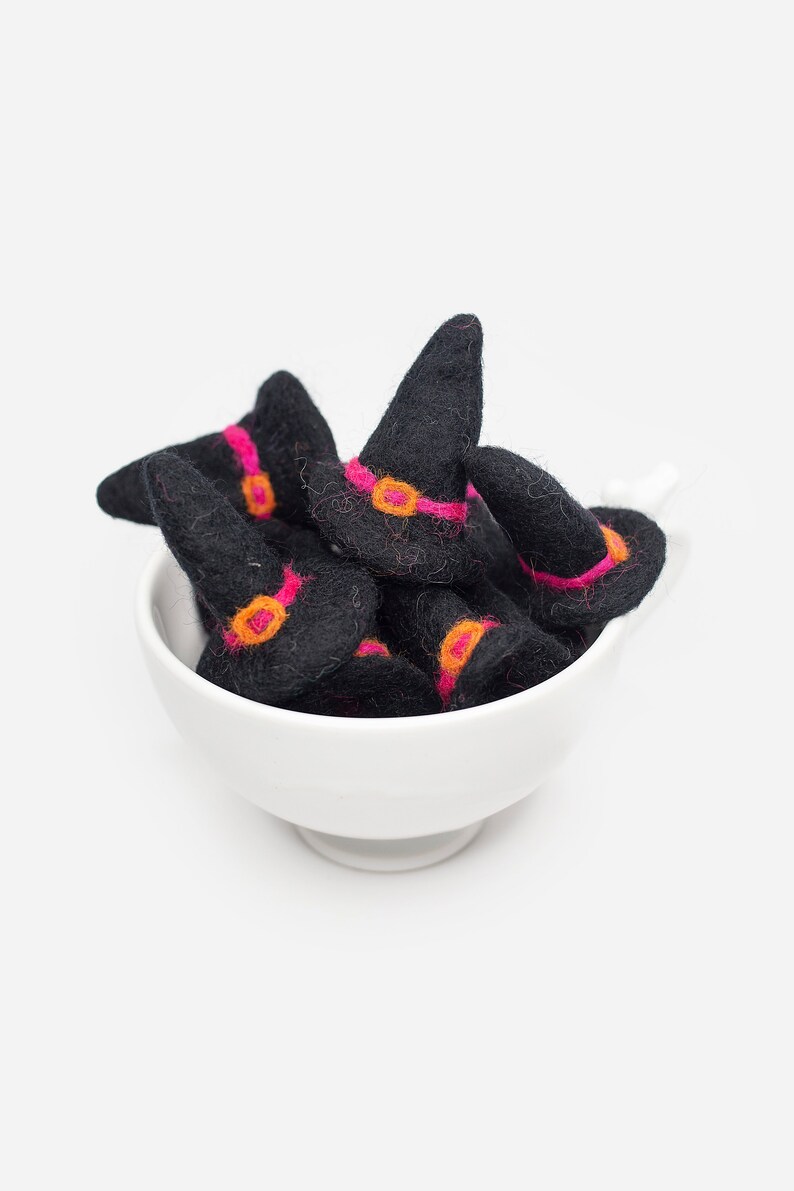 May include: A white ceramic bowl filled with black felt witch hats with pink and orange trim.