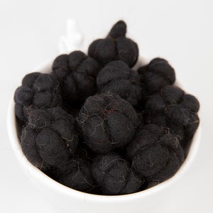 May include: A white bowl filled with black felt balls. The balls are round and have a slightly textured surface.