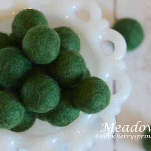 May include: A bowl filled with green felt balls. The bowl is white with a decorative edge. The text "Meadow @shopcherry sprinkles" is at the bottom of the image.