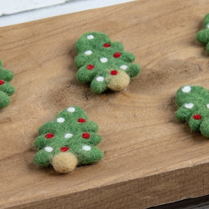 May include: Four felt Christmas tree decorations on a wooden surface. The trees are green with white and red felt dots.