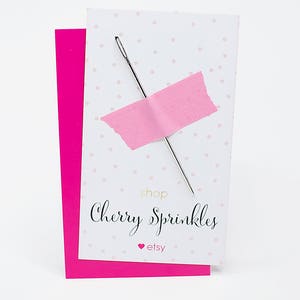 May include: A white card with pink polka dots and a pink piece of tape with a needle sticking through it. The card says "shop Cherry Sprinkles" and "etsy" in gold lettering.