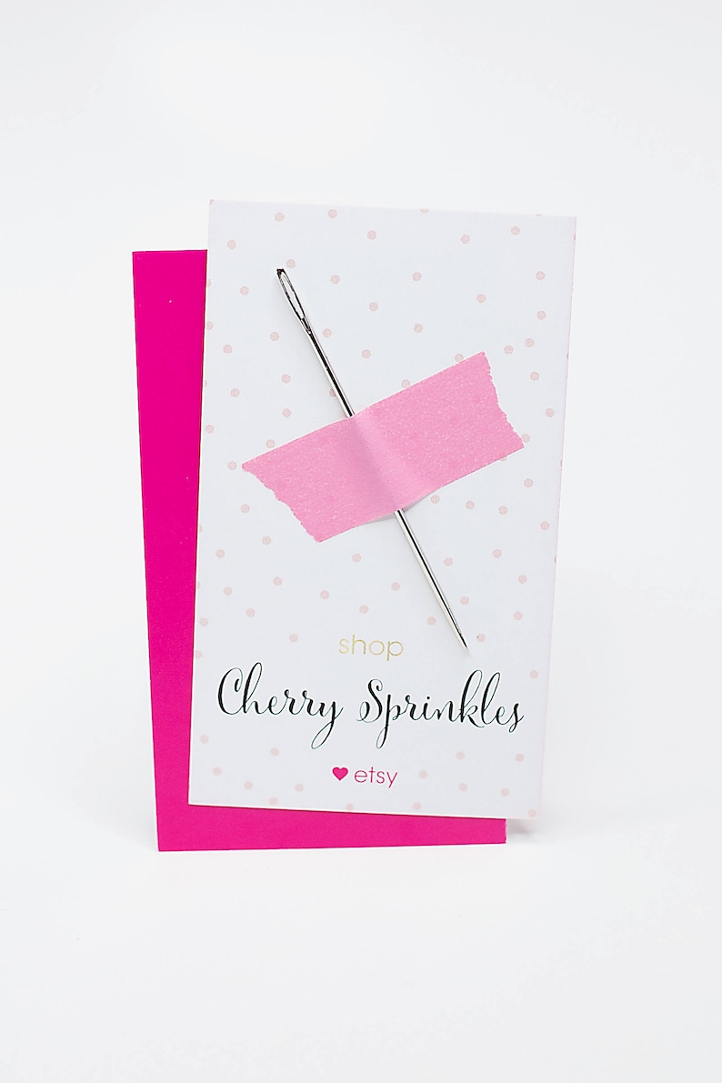 May include: A white card with pink polka dots and a pink piece of tape with a needle sticking through it. The card says "shop Cherry Sprinkles" and "etsy" in gold lettering.