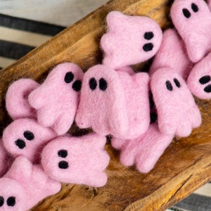 May include: A bowl filled with pink felt ghost decorations. The ghosts have black felt eyes and are arranged in a random pattern.