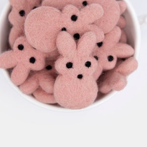 May include: A white ceramic bowl filled with pink felt bunny shapes. The bunnies have black eyes and noses.