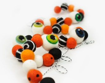 May include: A Halloween garland made of felt balls in orange, white, and black with googly eyes. The garland is strung together with twine.