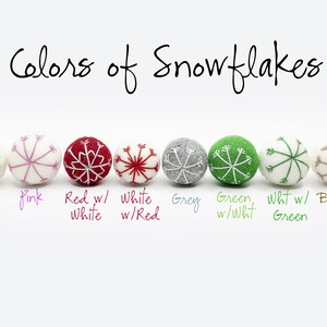 Puede incluir: Una fila de ocho adornos de fieltro con forma de copo de nieve, cada uno con un color y dise&ntilde;o diferente. Los colores son menta, rosa, rojo con blanco, blanco con rojo, gris, verde con blanco, blanco con verde y arpillera.