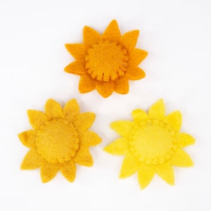 May include: Three felt flower embellishments in the shape of sunflowers. The flowers are yellow and orange with a textured felt finish.