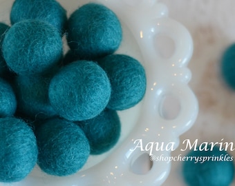 May include: A bowl of teal blue felt balls. The balls are soft and fluffy, and they are perfect for crafting or decorating.