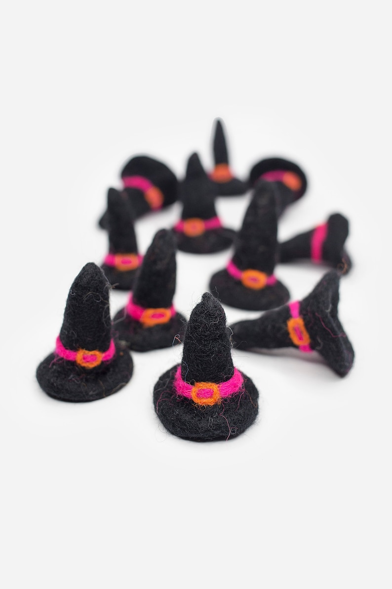 May include: A group of black felt witch hats with pink and orange trim. The hats are arranged in a circle on a white background.