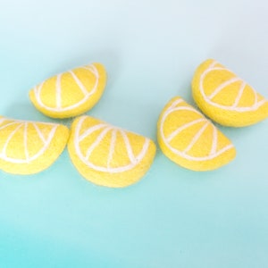 May include: Five felt lemon slices with white detailing on a light blue background. The lemon slices are bright yellow with white segments, creating a cheerful and vibrant display. These could be used for crafting or decoration.