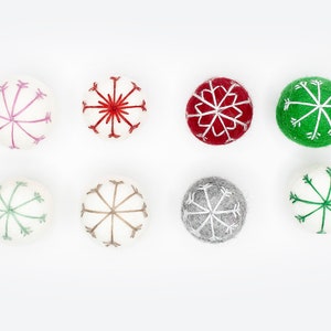 Puede incluir: Ocho adornos de fieltro con dise&ntilde;os de copos de nieve en varios colores, incluyendo rojo, verde, rosa, gris y blanco.