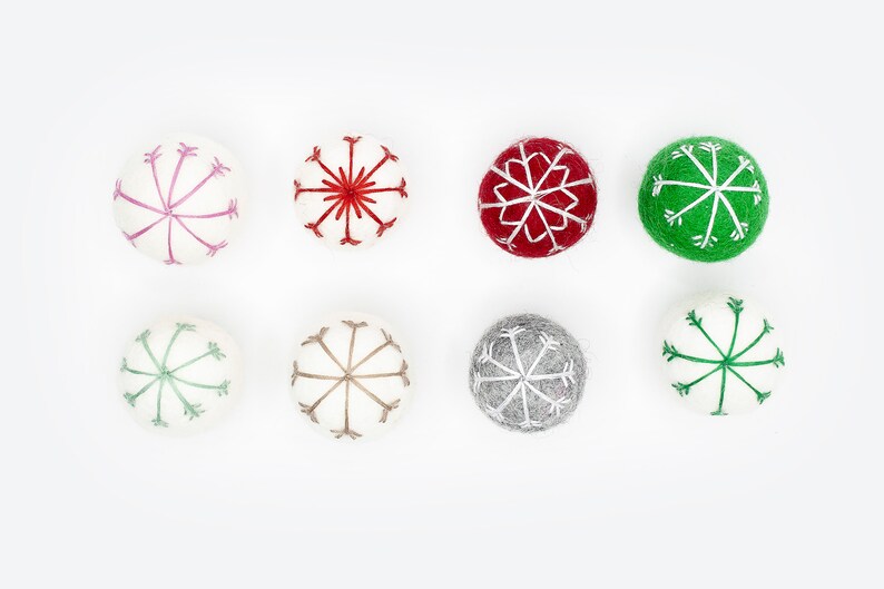 Puede incluir: Ocho adornos de fieltro con dise&ntilde;os de copos de nieve en varios colores, incluyendo rojo, verde, rosa, gris y blanco.