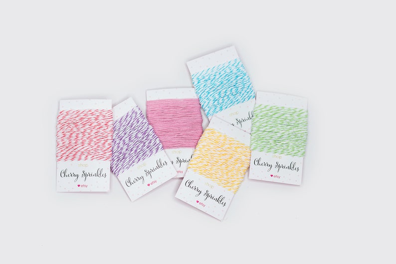 May include: An overhead shot displays six spools of twine in various colors: red, purple, pink, yellow, blue, and green. Each spool is labeled "Cherry Sprinkles" with the Etsy logo. The twine is neatly wound on white cards with a dotted pattern.
