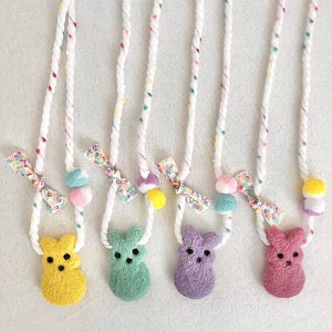 May include: Five colorful felt necklaces with a fuzzy bear charm. Each necklace has a white rope with colorful stripes and a small bow.