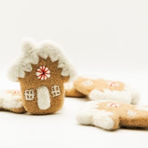 May include: A felt gingerbread house and gingerbread men with white frosting and red and white candy accents. The house has a white roof and a red and white candy in the center. The gingerbread men are scattered around the house.