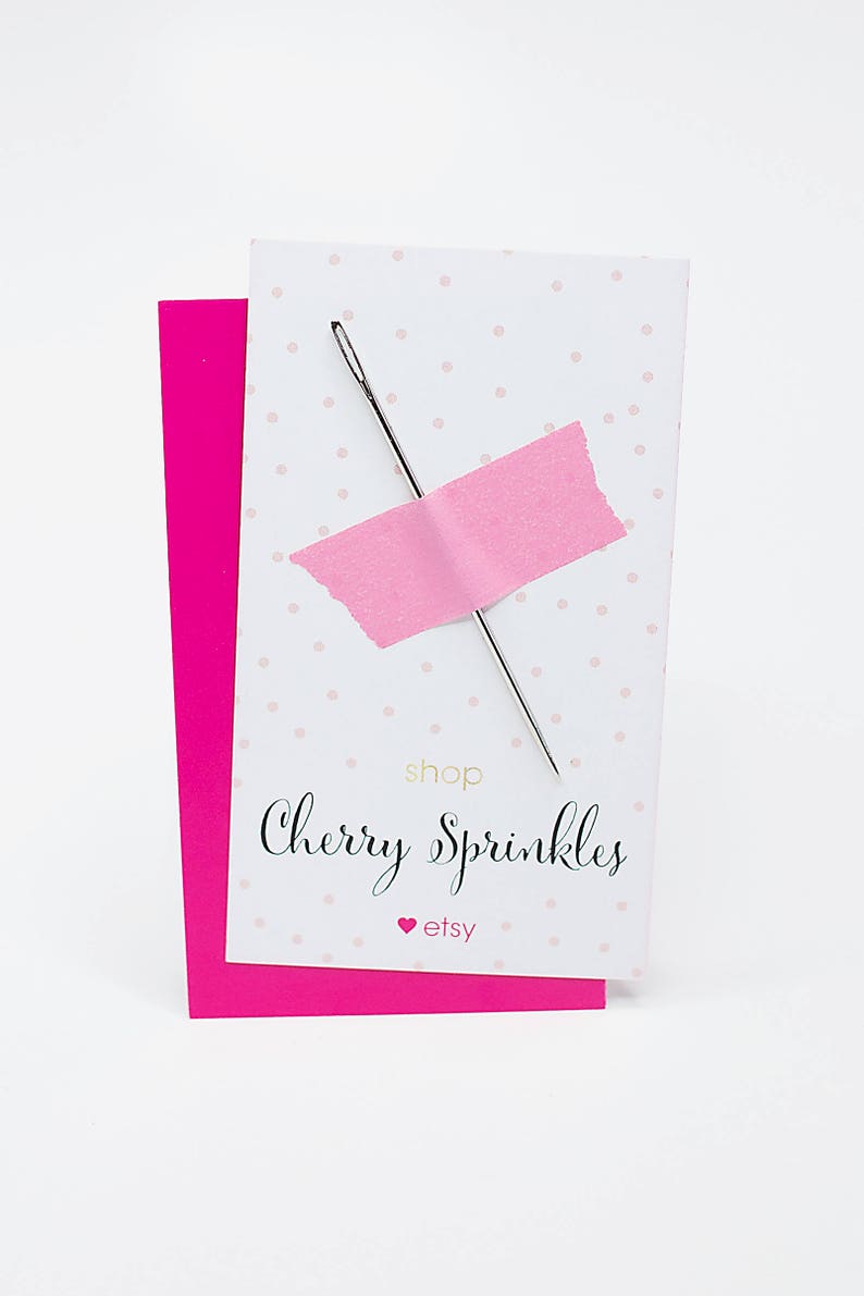 May include: A silver needle is taped to a white card with pink polka dots. The card is labeled "shop Cherry Sprinkles" with a pink heart and the Etsy logo. A bright pink card is behind the white card.