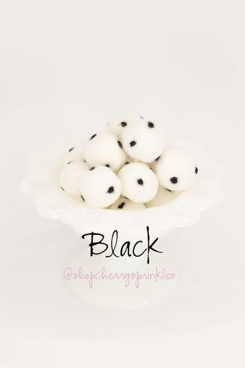 May include: A white bowl filled with white pom poms with black polka dots. The text "Black" is written below the bowl. The text "@shopcherryssprinkles" is written below the word "Black".