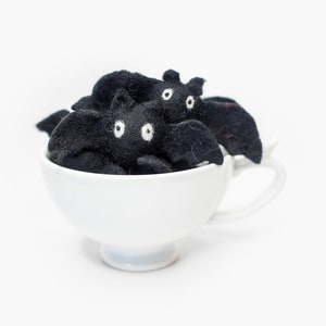 May include: A white teacup filled with black felt bats with white eyes. The bats are arranged in a cluster, with their wings spread out.