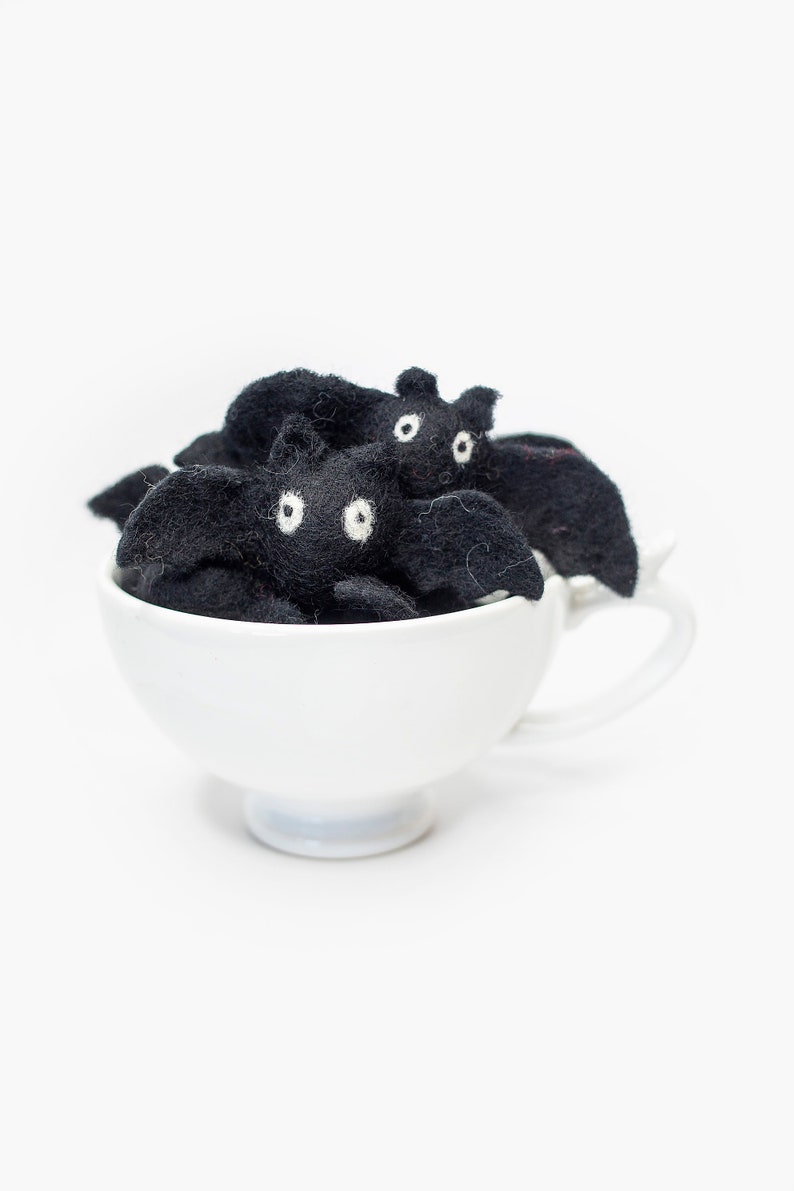 May include: A white teacup filled with black felt bats with white eyes. The bats are arranged in a cluster, with their wings spread out.