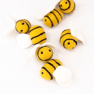 May include: Six felt bee ornaments with black stripes and smiling faces. The bees have white felt wings.