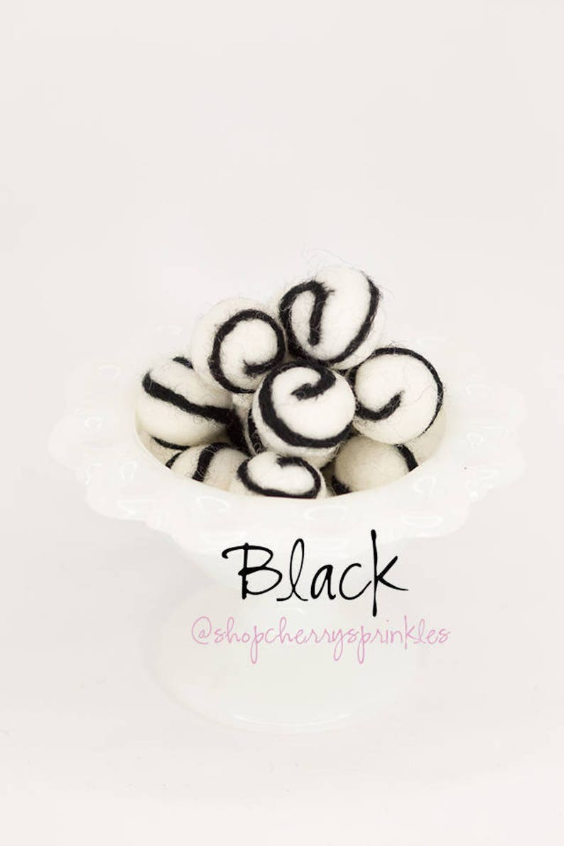 May include: A white bowl filled with white felt balls with black swirl designs. The text "Black" and "@shopcherryssprinkles" is below the bowl.