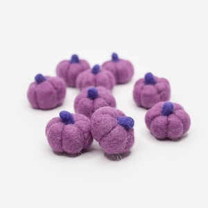 May include: A group of eight small purple felt pumpkins with blue stems. The pumpkins are arranged in a semi-circle on a white background.