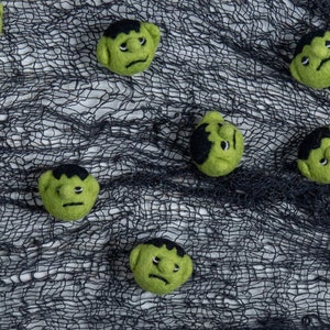 Pu&ograve; includere: Volti di mostri in feltro verde con capelli e sopracciglia neri su uno sfondo di rete nera.