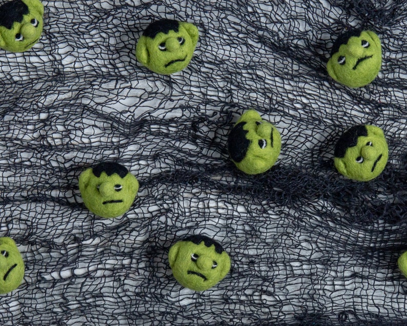 Pu&ograve; includere: Volti di mostri in feltro verde con capelli e sopracciglia neri su uno sfondo di rete nera.