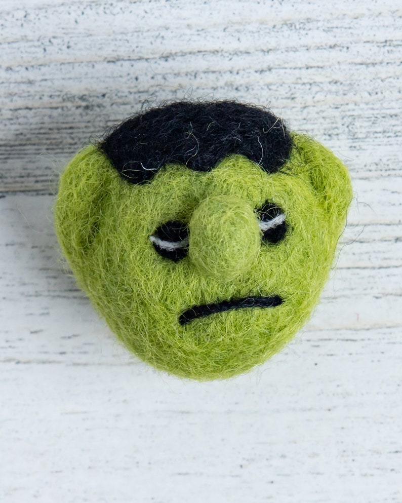 Pu&ograve; includere: Mostro di feltro verde con capelli di feltro nero e un'espressione triste.