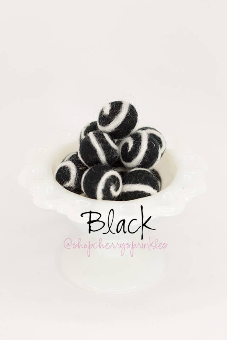 May include: A white bowl filled with black and white felt balls. The balls have a swirl pattern. The text "Black" and "@shopcherryssprinkles" is below the bowl.