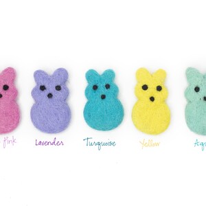 May include: Five felt bunny shapes in different colors: rose pink, lavender, turquoise, yellow, and aqua. Each bunny has black eyes and a simple, smiling expression.