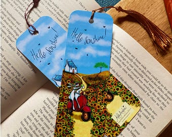 Könnte beinhalten: Zwei rechteckige Lesezeichen aus Papier mit blauem Himmel, dem Text Hello Sunshine, einem weißen Haus und einem Sonnenblumenfeld. Ein Lesezeichen zeigt zwei Figuren auf einem roten Roller, beide haben ein Loch oben mit einer Seidenquaste.