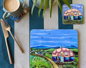 Könnte beinhalten: Ein quadratischer Untersetzer und ein kleinerer quadratischer Untersetzer, beide mit einer bunten Illustration eines rosa-blauen Wohnwagens in einer grünen Landschaft und dem Text Life is better with friends, dazu ein grauer Becher und silbernes Besteck.