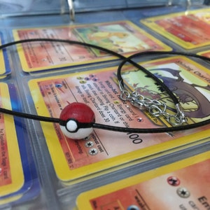Op de afbeelding: Een zwarte koordketting met een zilveren sluiting en een rode en witte Pok&eacute;bal-bedel.