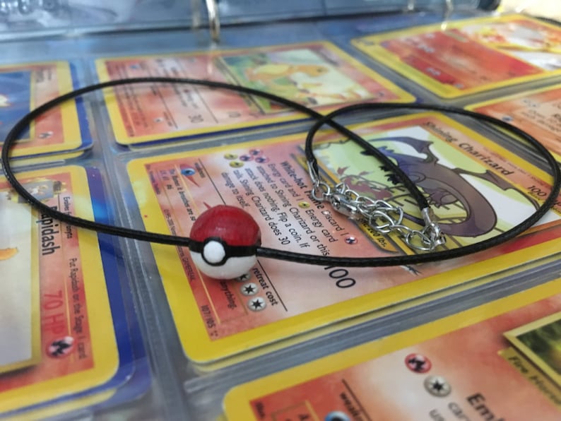 Op de afbeelding: Een zwarte koordketting met een zilveren sluiting en een rode en witte Pok&eacute;bal-bedel.