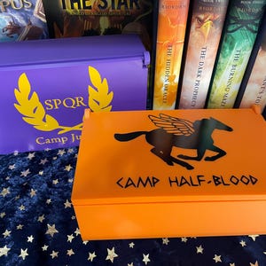 May include: Two wooden boxes, one purple with a gold laurel wreath and the letters "SPQR" and the words "Camp Jupiter", and the other orange with a black Pegasus and the words "Camp Half-Blood".