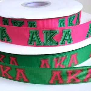 May include: Two rolls of ribbon with the letters "AKA" printed on them. The top roll is pink with green letters and the bottom roll is green with pink letters.