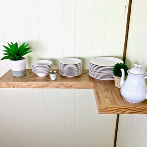 Puede incluir: Una estanter&iacute;a de esquina de madera con una tetera blanca, una suculenta en maceta y pilas de platos blancos.